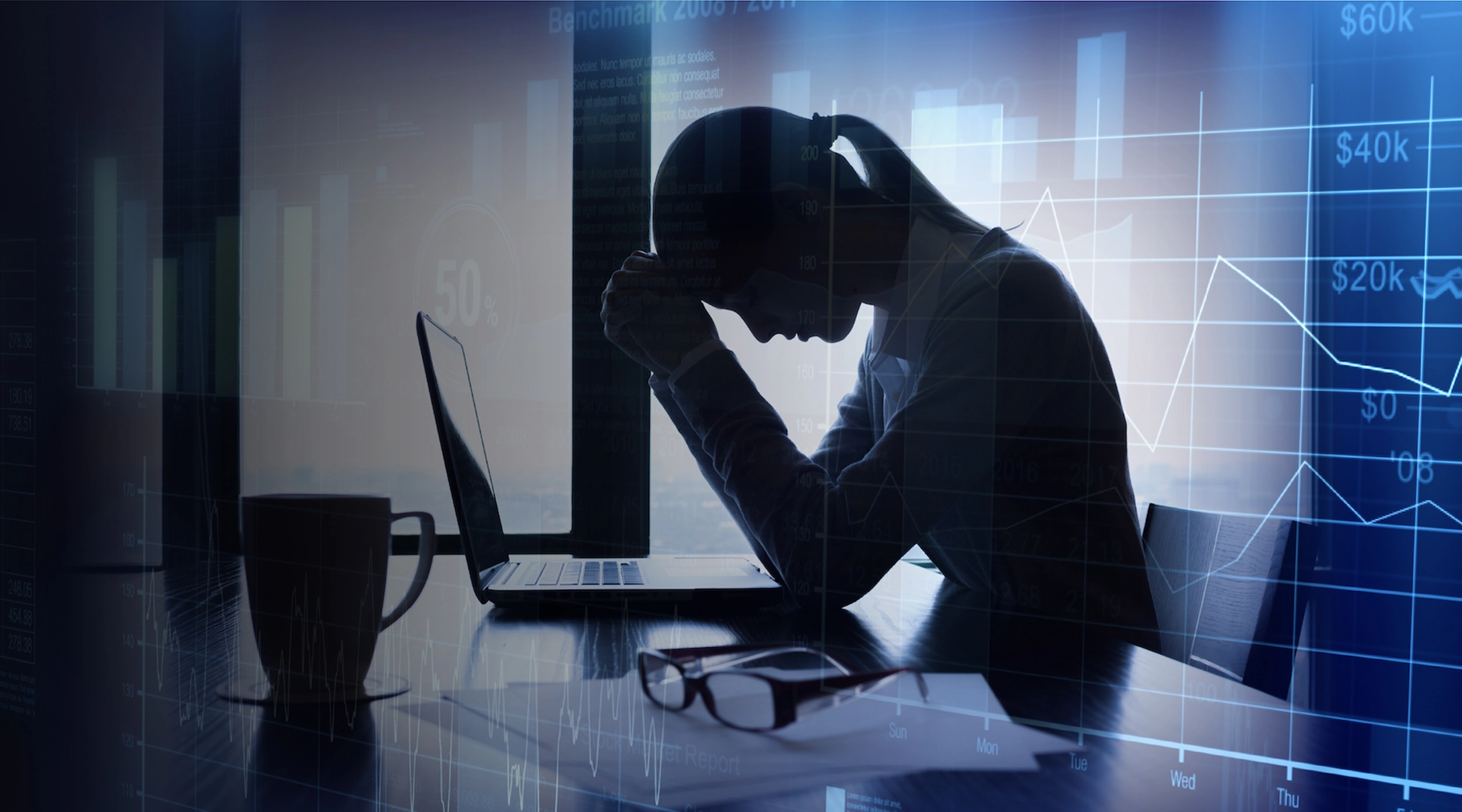 Woman holding her head down sitting at a desk with a laptop. Line graph graphic in foreground.