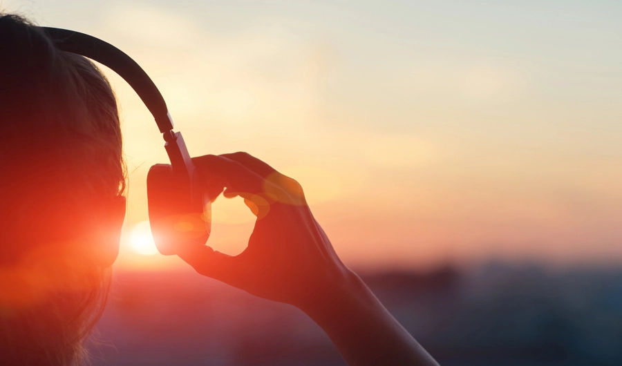 Woman wearing headphones looking at sunset.